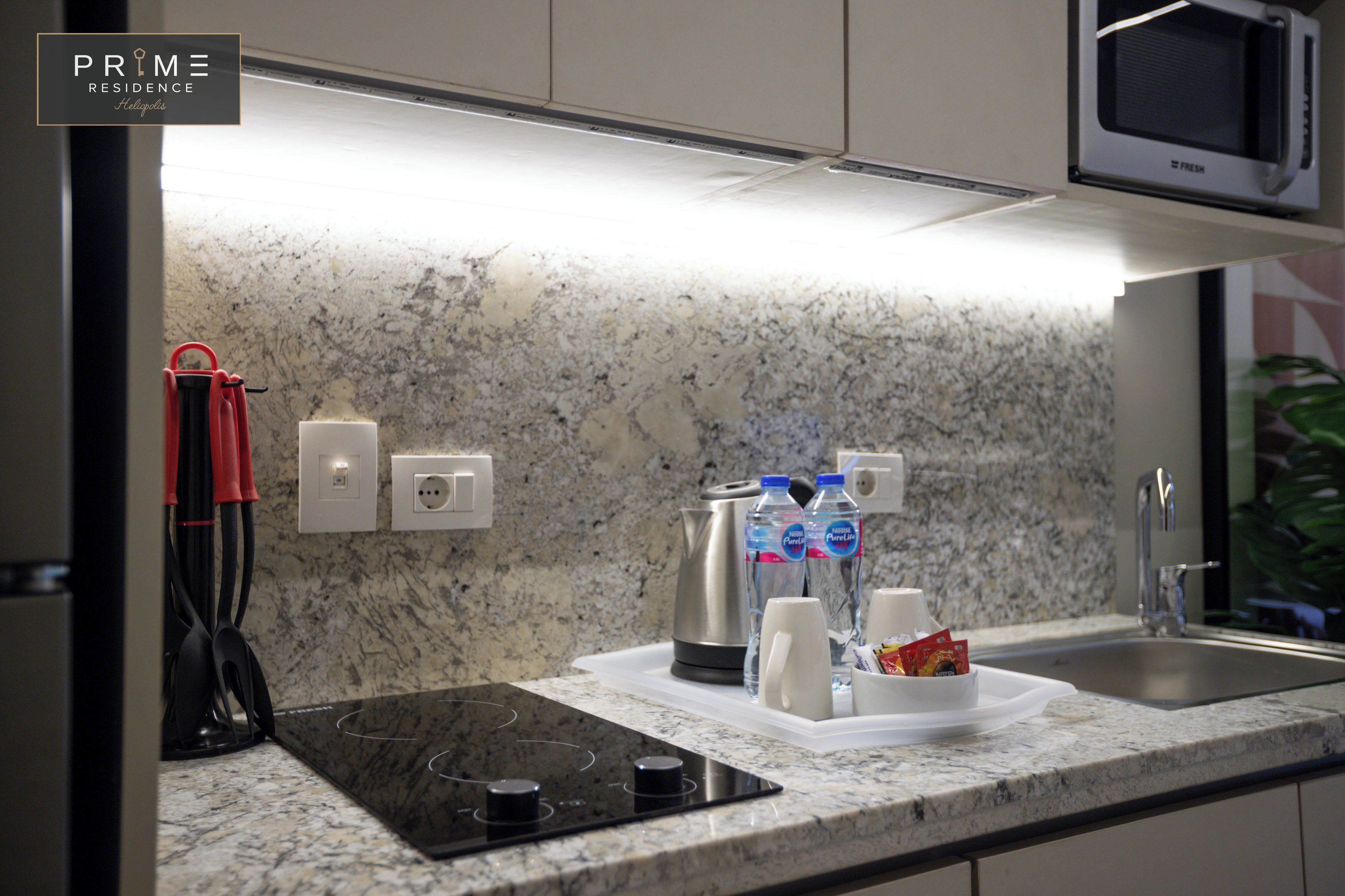 A modern kitchen with granite countertops, a built-in microwave, a kettle, and a coffee maker.
