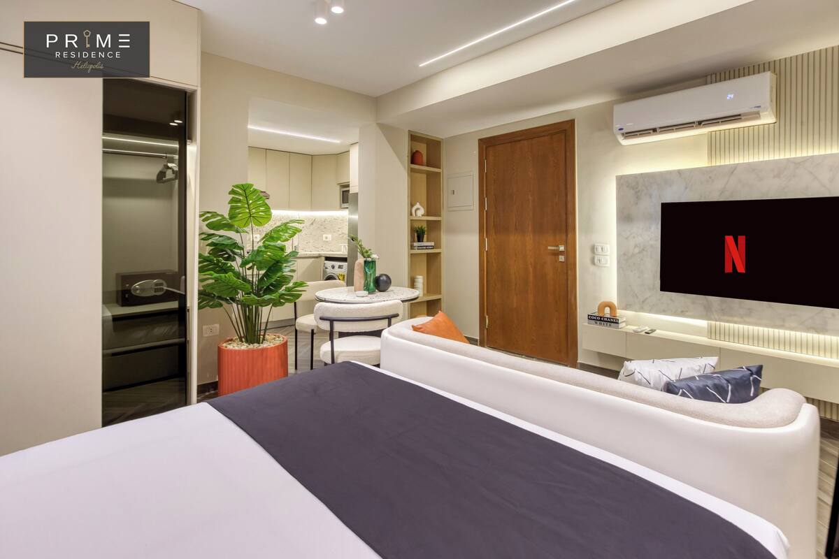 Una habitación de hotel moderna con cama, televisor, una mesita redonda y una planta en maceta.