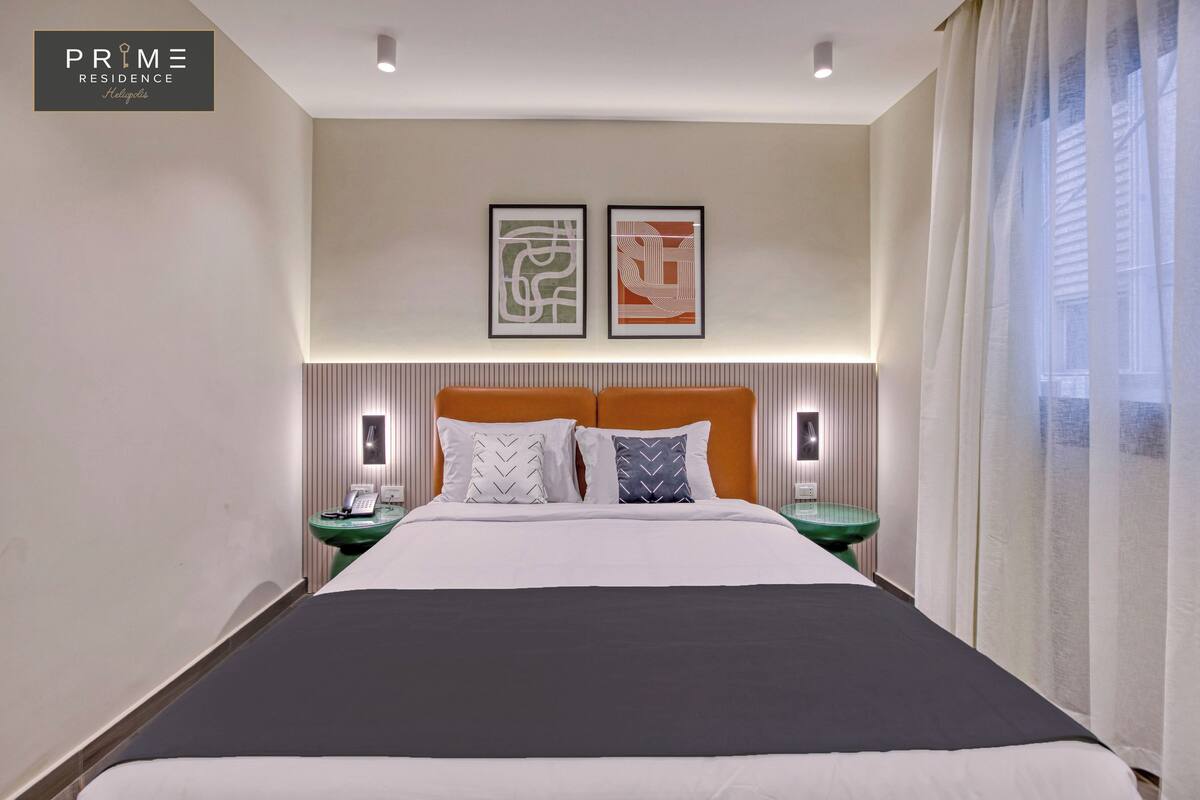 Habitación de hotel con una cama grande, dos mesitas de noche con lámparas, y dos obras de arte abstracto enmarcadas en la pared.