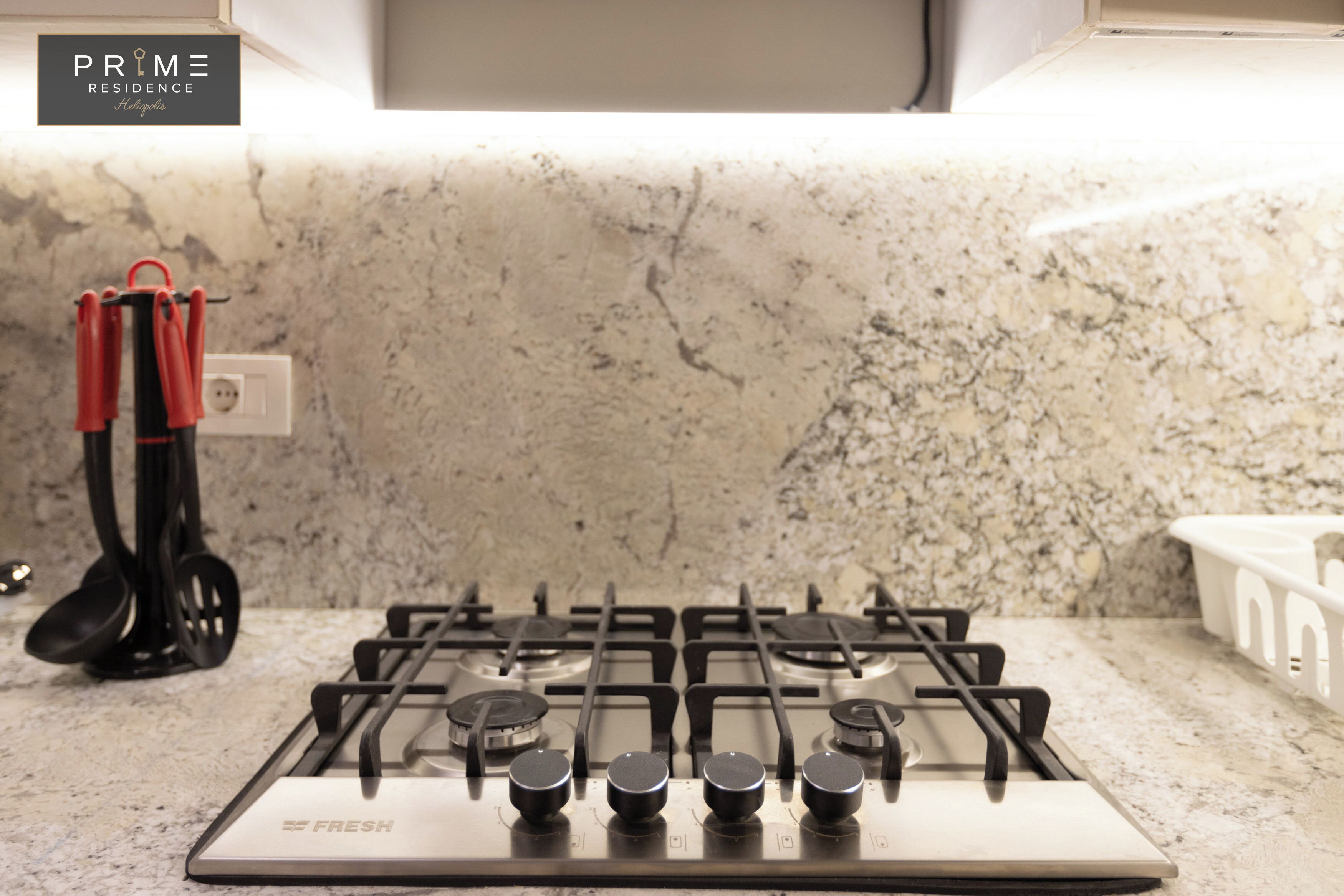 A kitchen with a gas stove, a marble countertop, and a hanging pot rack.