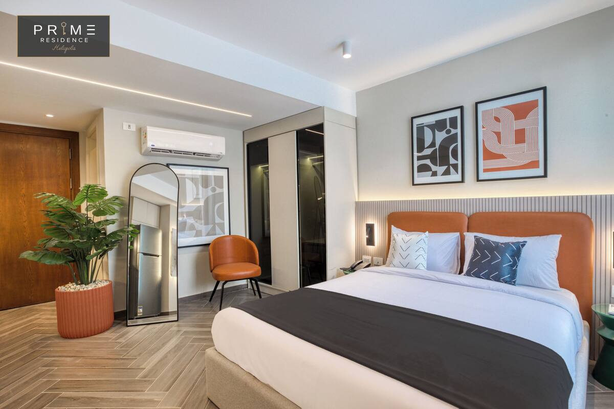 Una habitación de hotel moderna con una cama grande, una planta en maceta, un espejo y un armario.