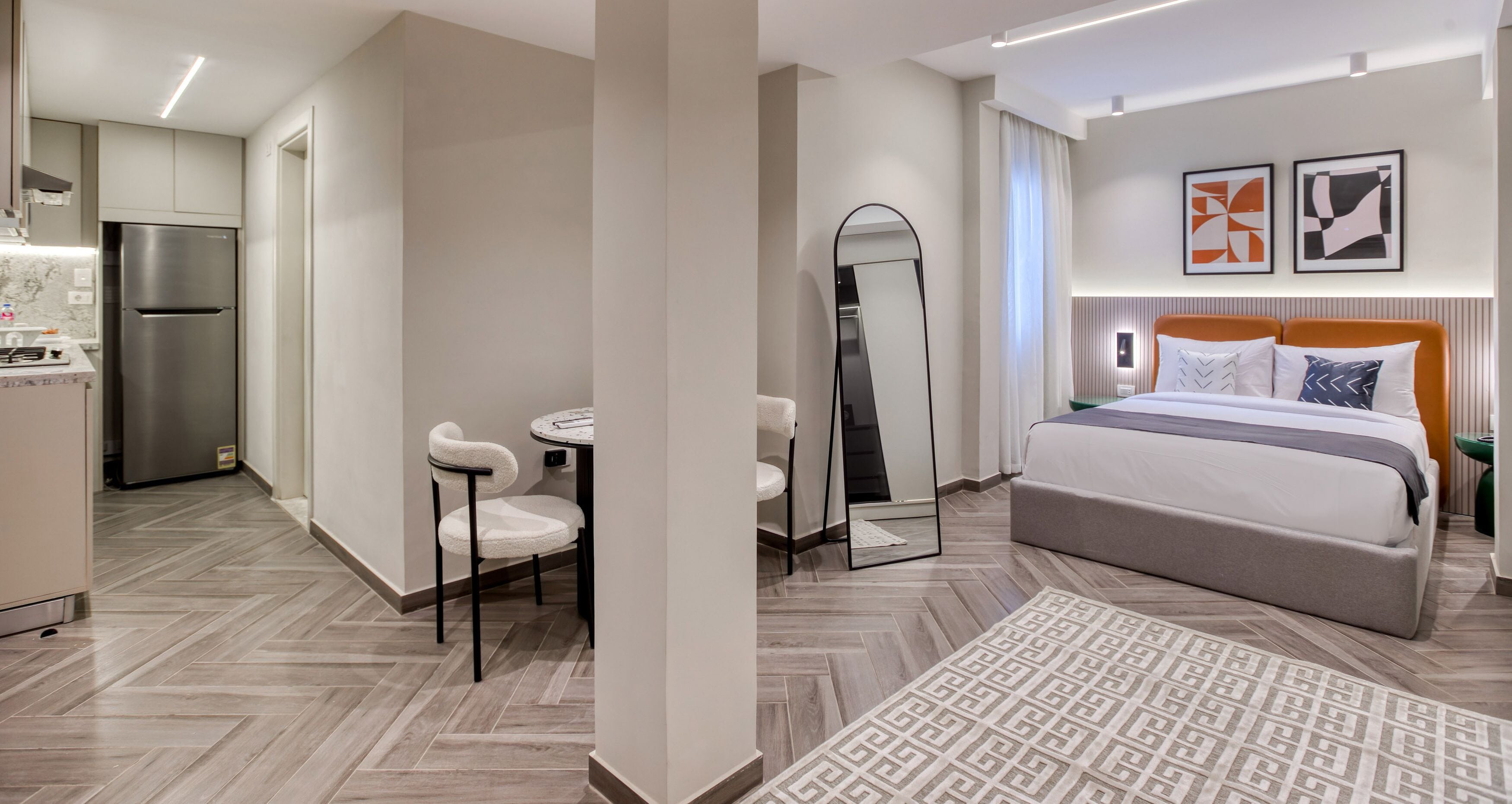 A modern hotel room with a bed, bedside table, and a small sitting area with chairs.