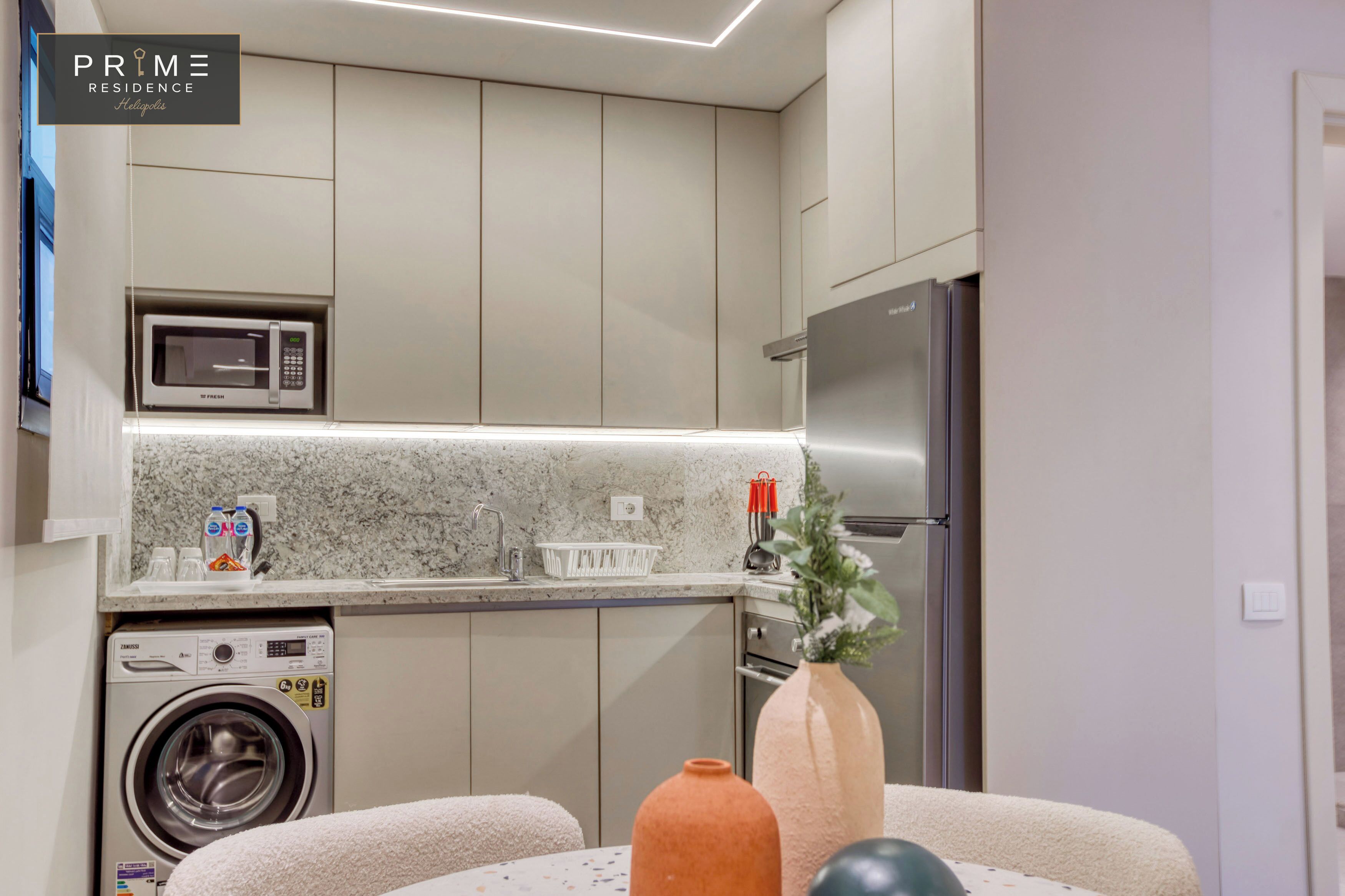 A modern kitchen with a built-in microwave, stainless steel refrigerator, and a washing machine.