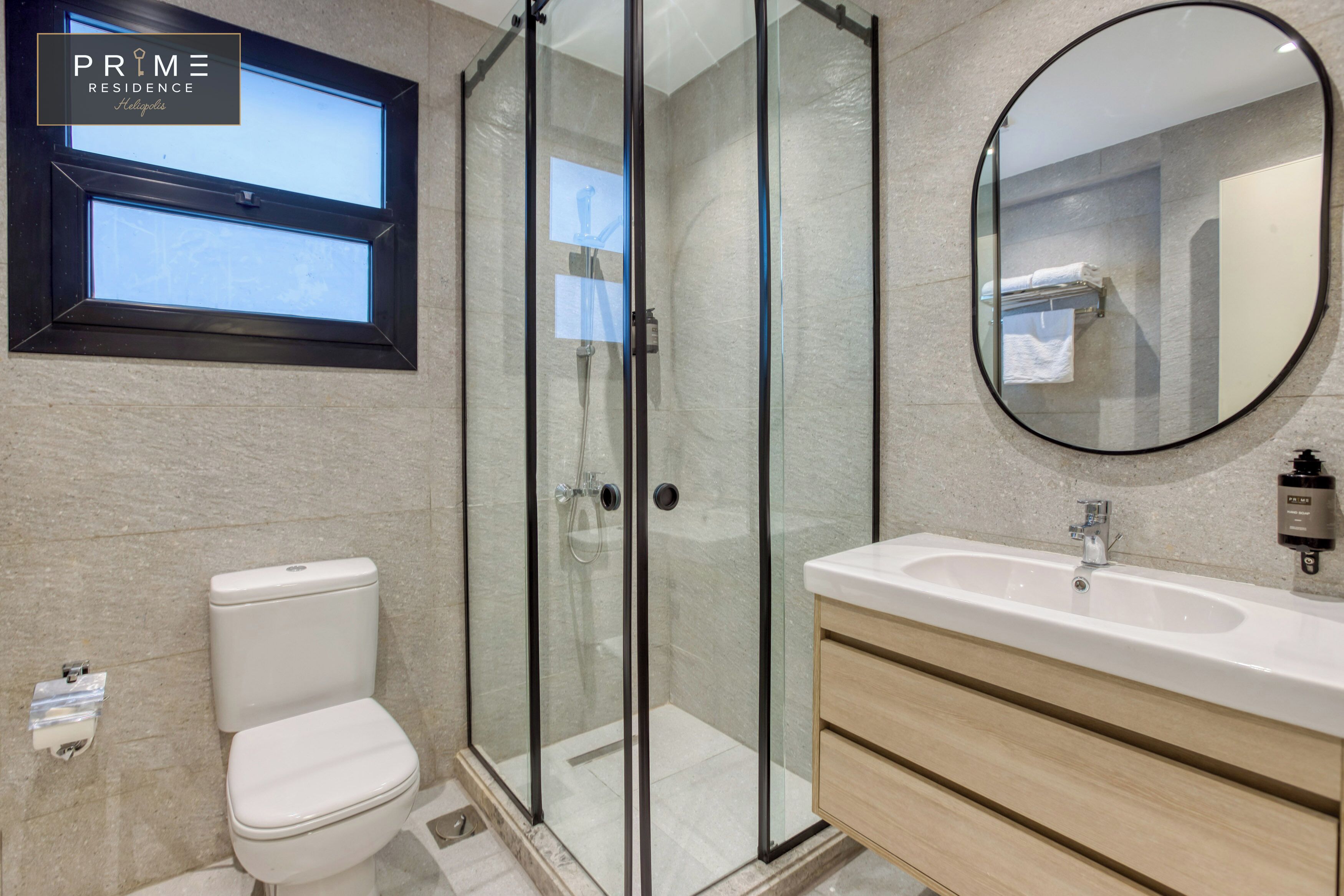 A modern bathroom with a glass-enclosed shower, a toilet, a sink with a mirror, and a window above the toilet.