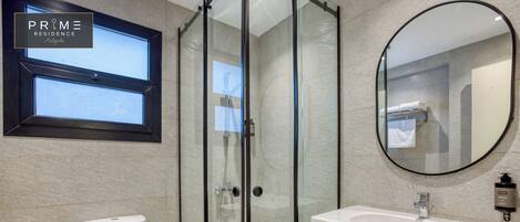 A modern bathroom with a glass-enclosed shower, a toilet, a sink with a mirror, and a window above the toilet.