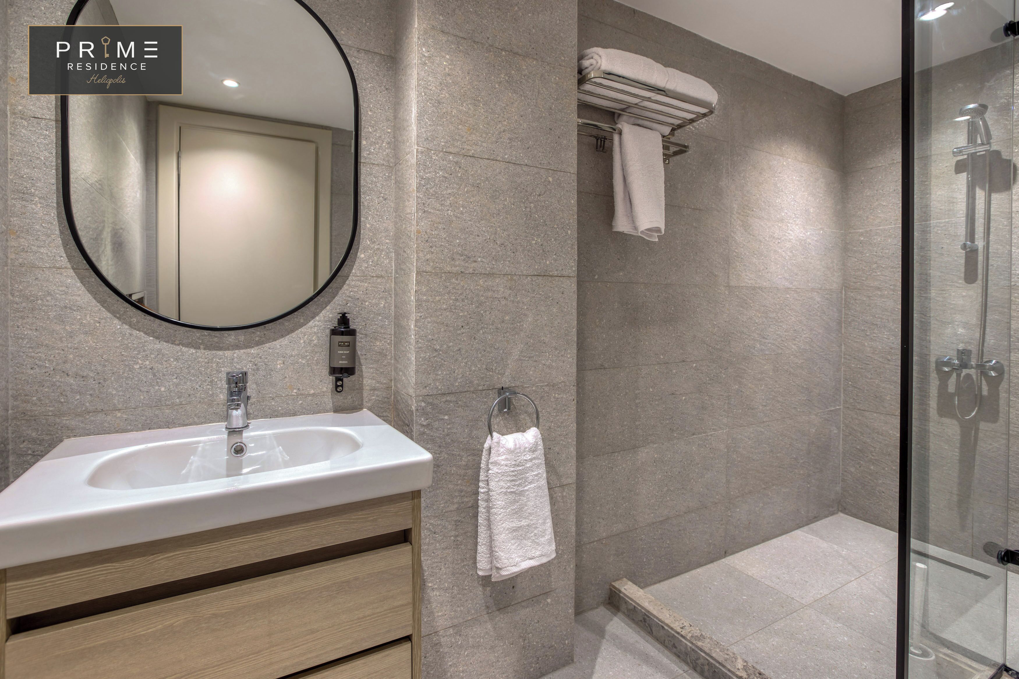 A modern bathroom with a sink, mirror, towel rack, and glass shower enclosure.