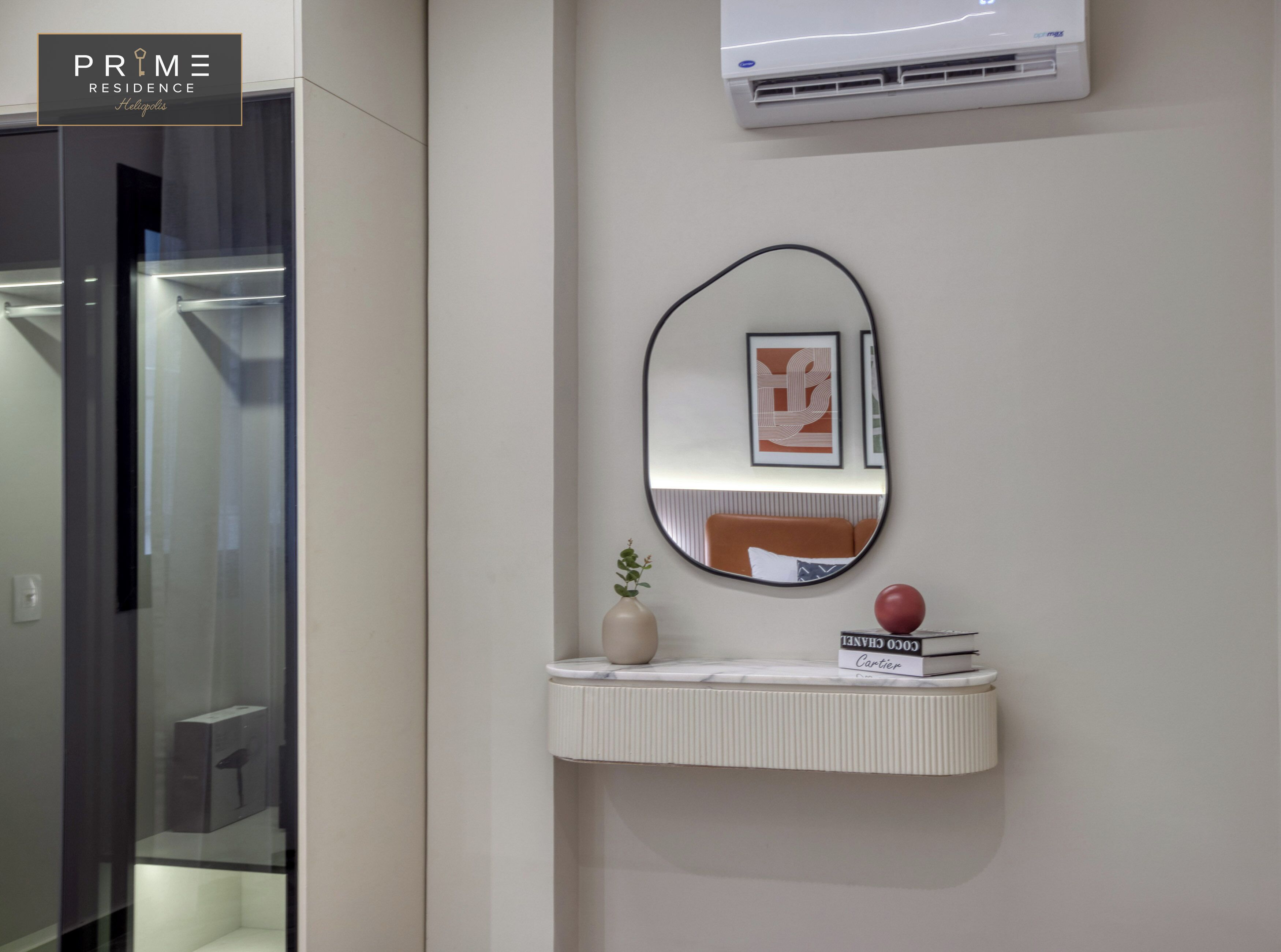 L’intérieur moderne d’un hôtel, avec un mur blanc, un miroir fixé au mur, une petite étagère blanche ornée d’un vase et de livres, et un appareil de climatisation.