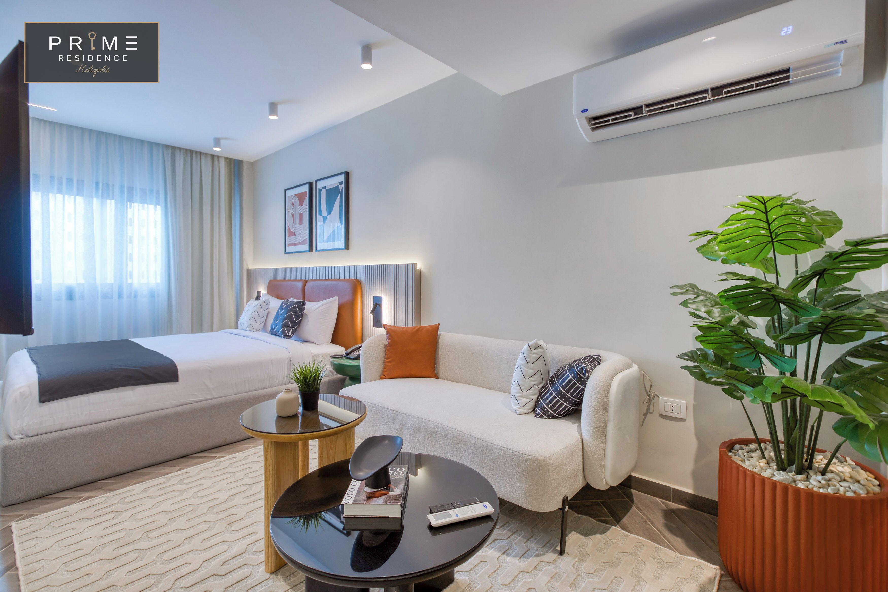 A modern hotel room with two beds, a sofa, a coffee table, and a large potted plant.