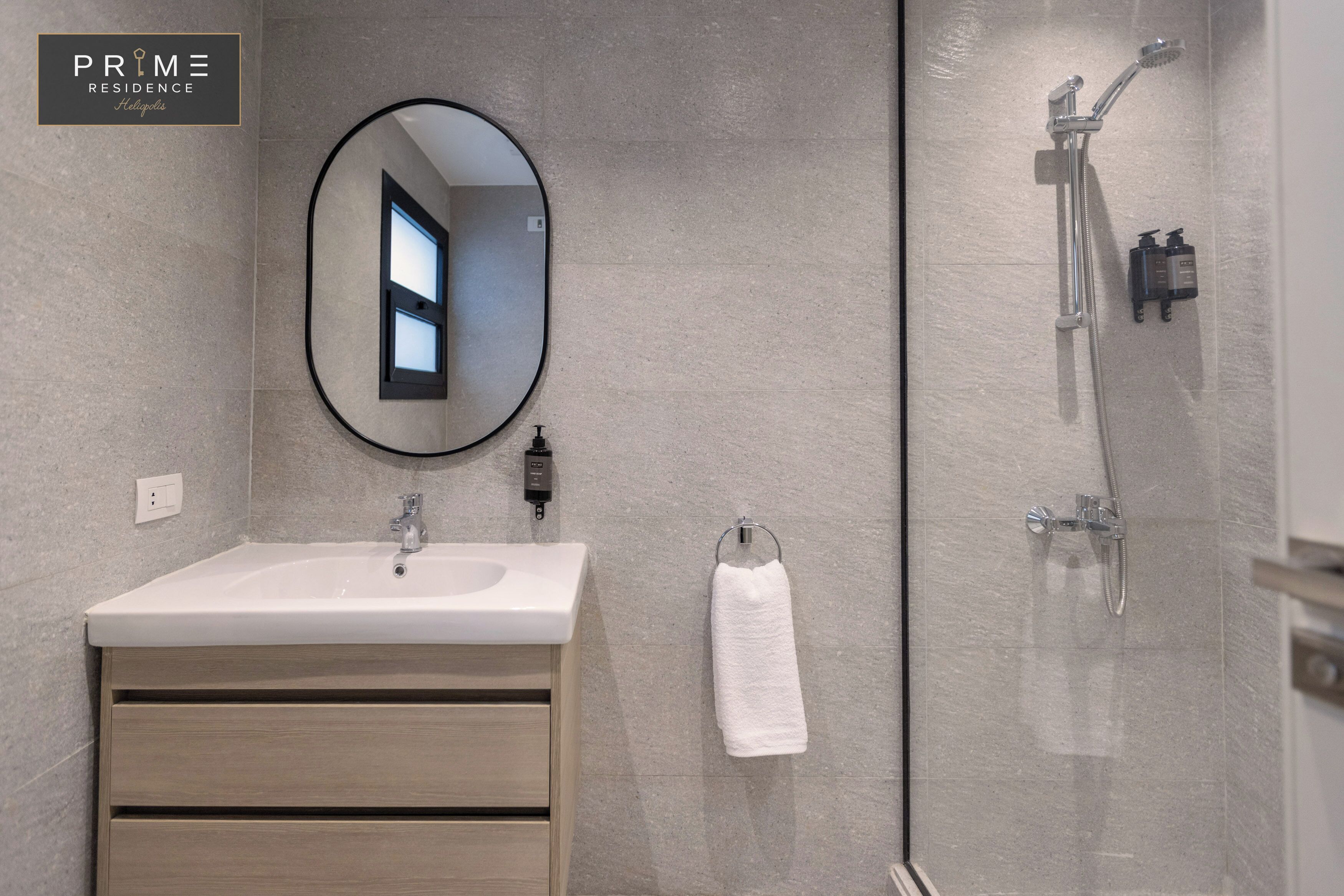 A modern bathroom with a white sink, a mirror, a towel rack, and a glass-enclosed shower area.