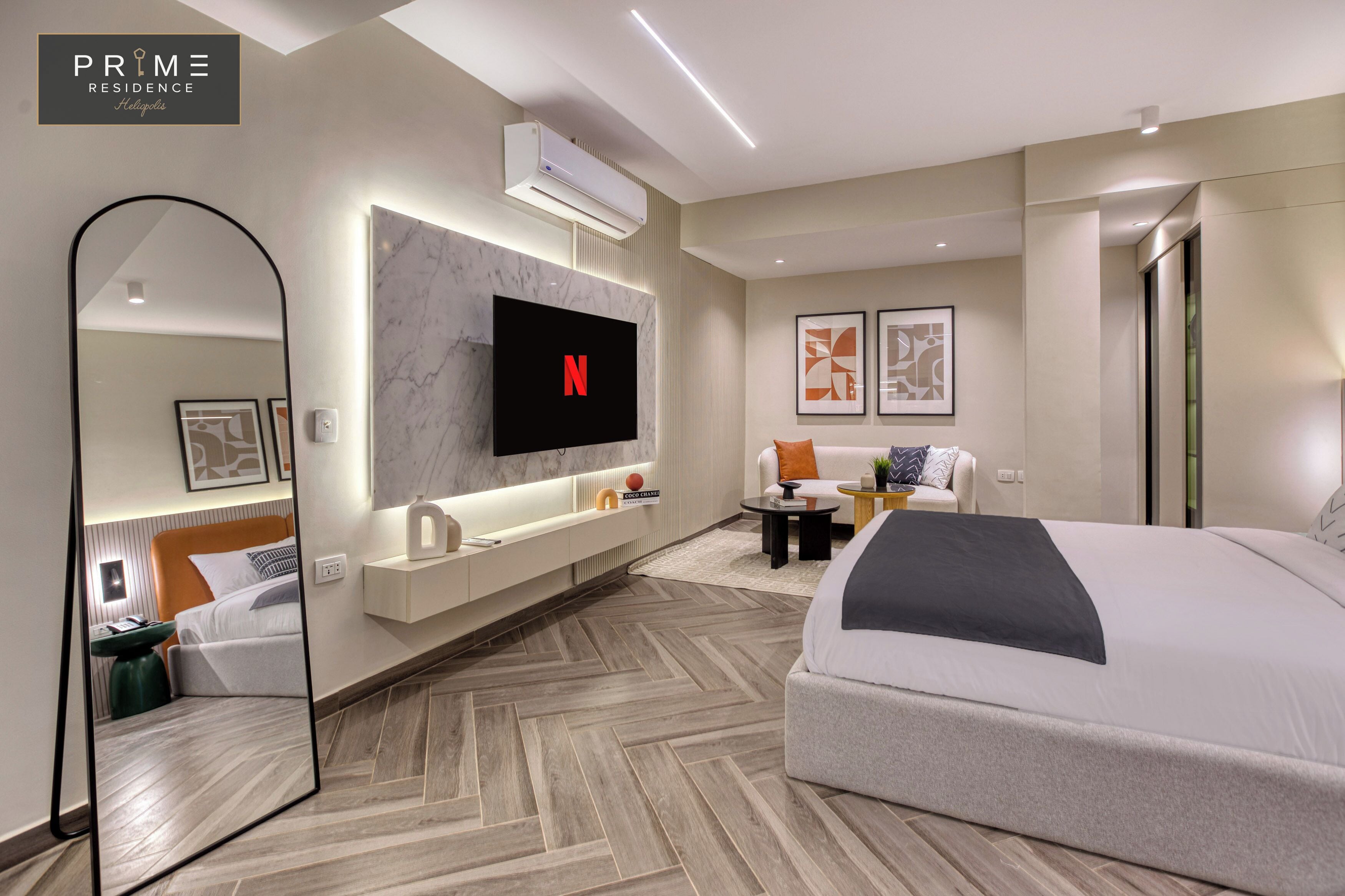Una camera d'albergo moderna con un letto grande, una TV a muro, uno specchio e un angolo salotto con un tavolino.