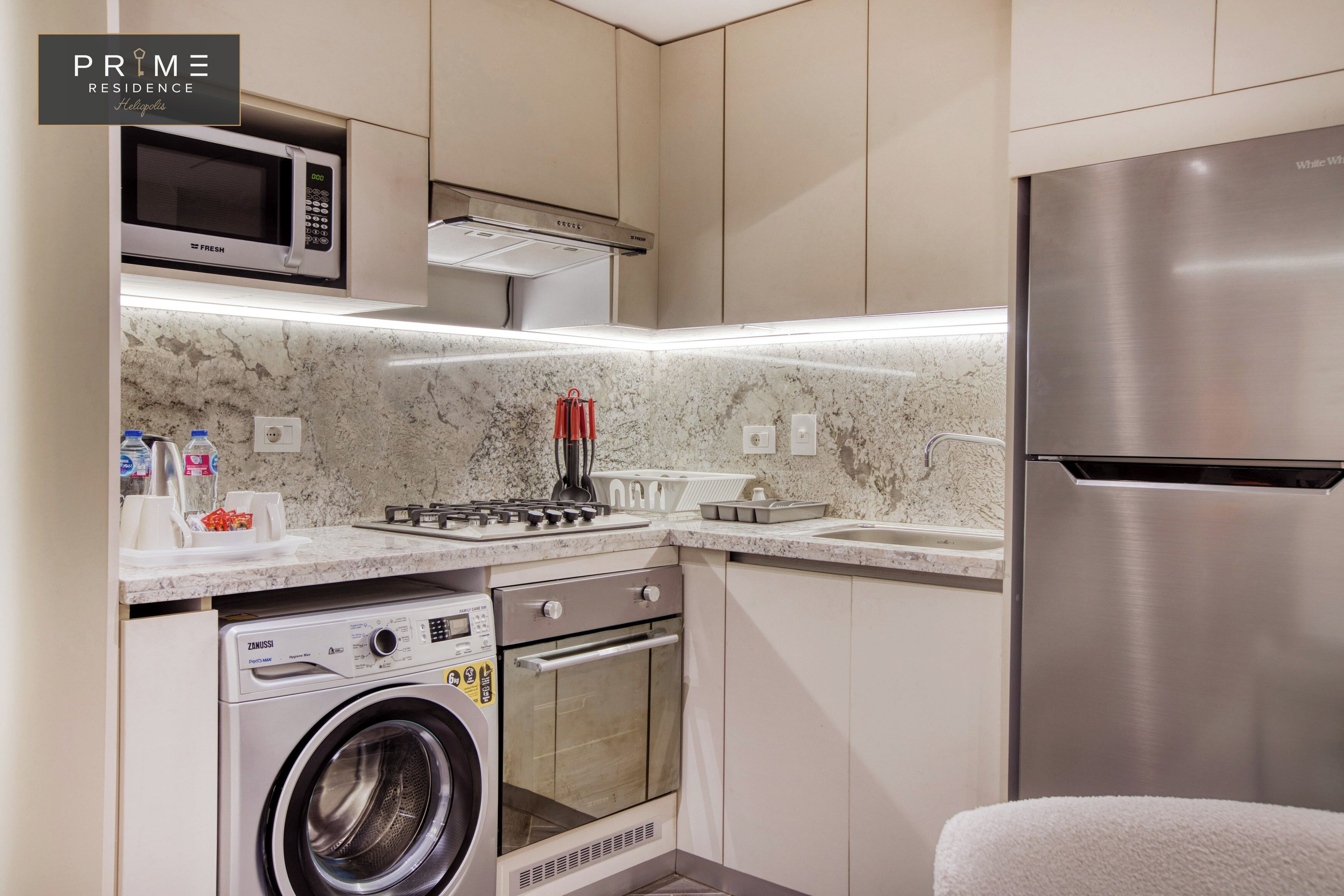 A modern kitchen with a stainless steel refrigerator, a built-in microwave, a washing machine, and a stove.