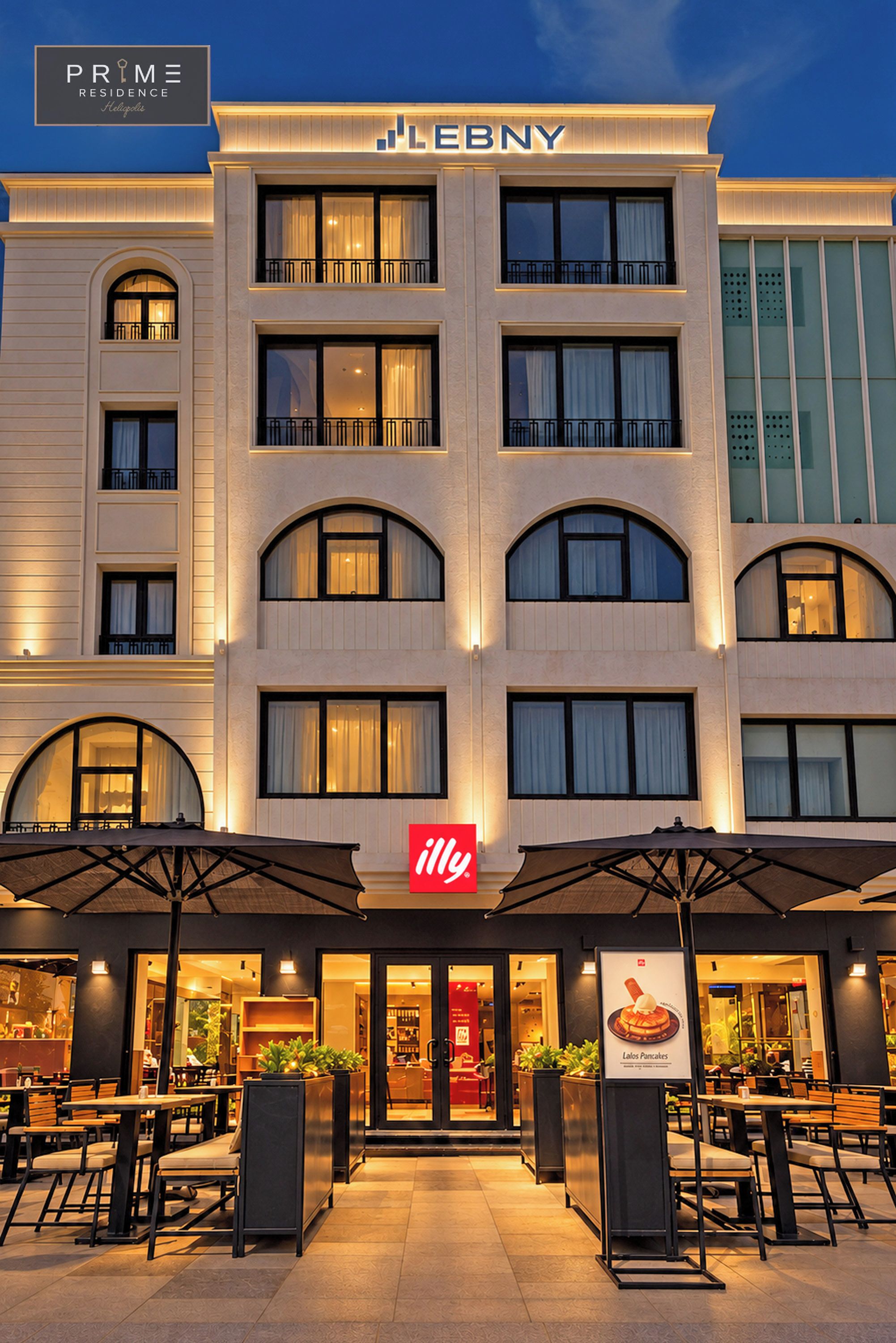 Un hotel LEBNY con un llamativo letrero rojo de 'illy', mesas al aire libre y una fachada bien iluminada.