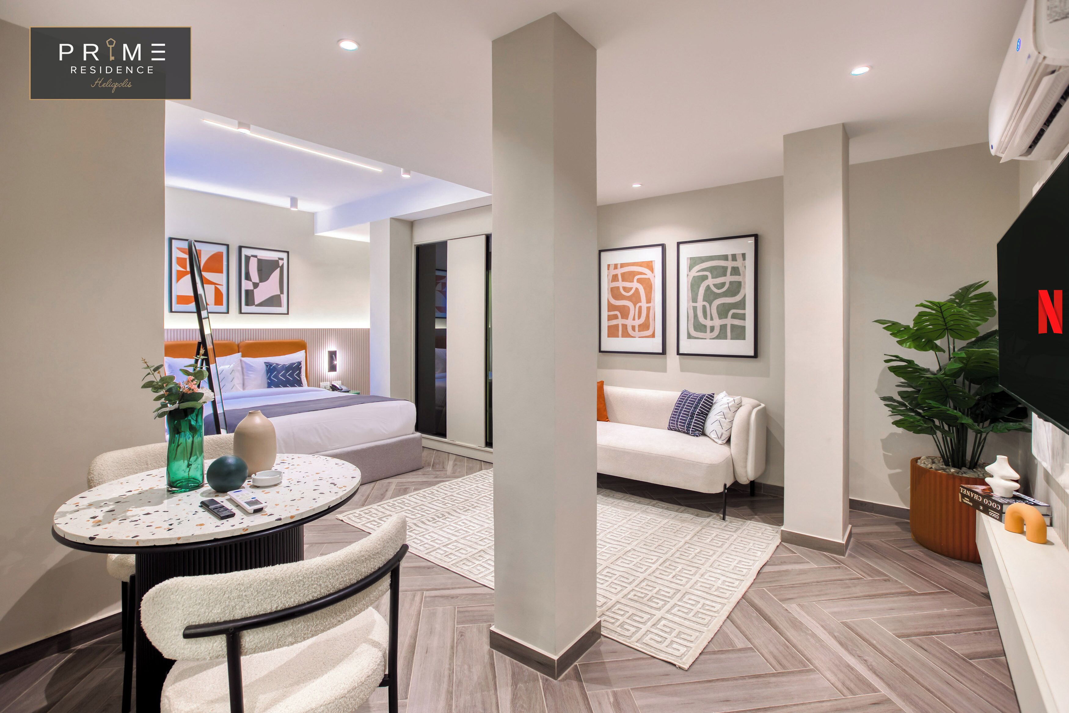 Quarto de hotel moderno com cama, sofá, mesa redonda e obras de arte nas paredes.