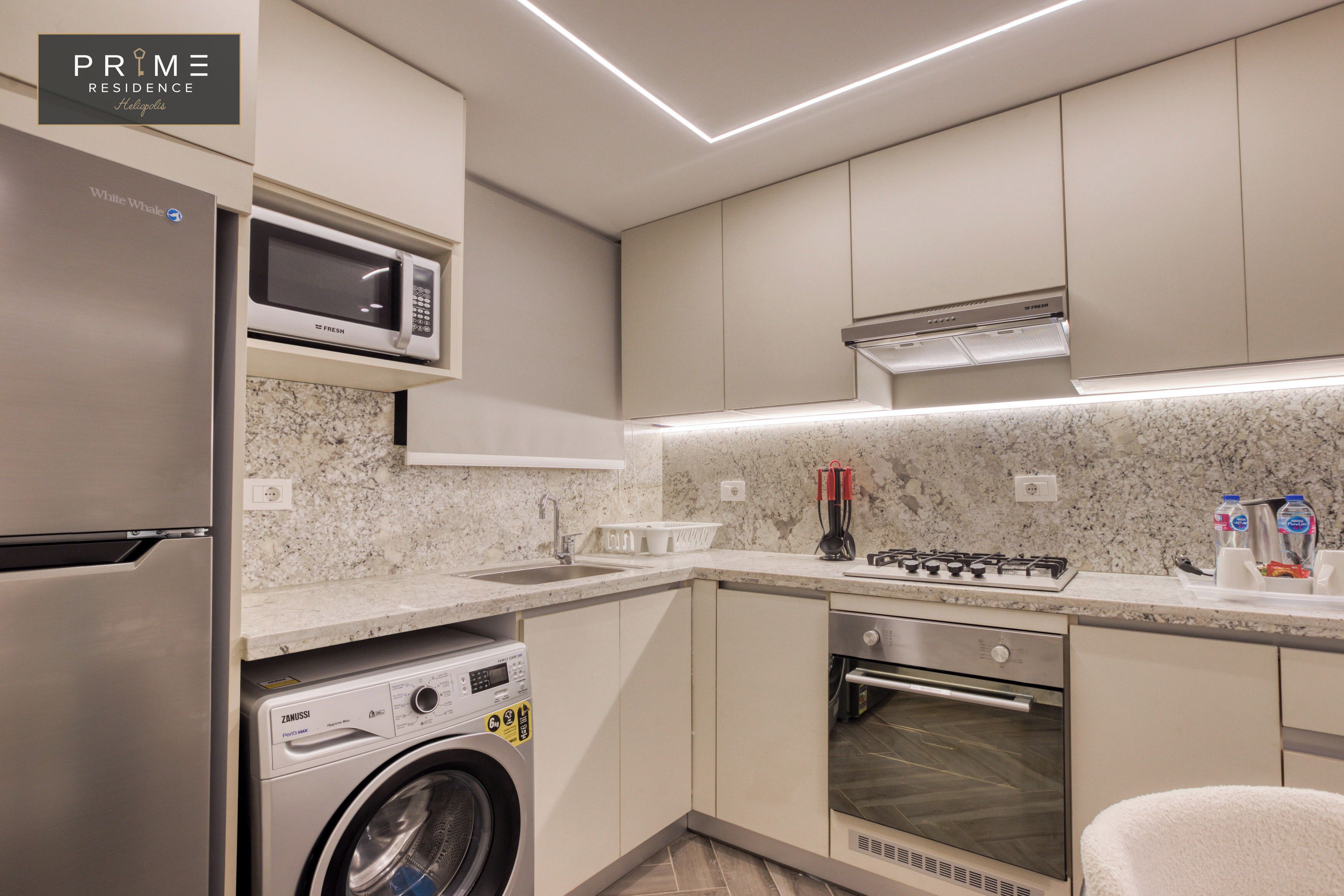 A modern kitchen with a stainless steel refrigerator, a microwave, a washing machine, an oven, and a gas stove.
