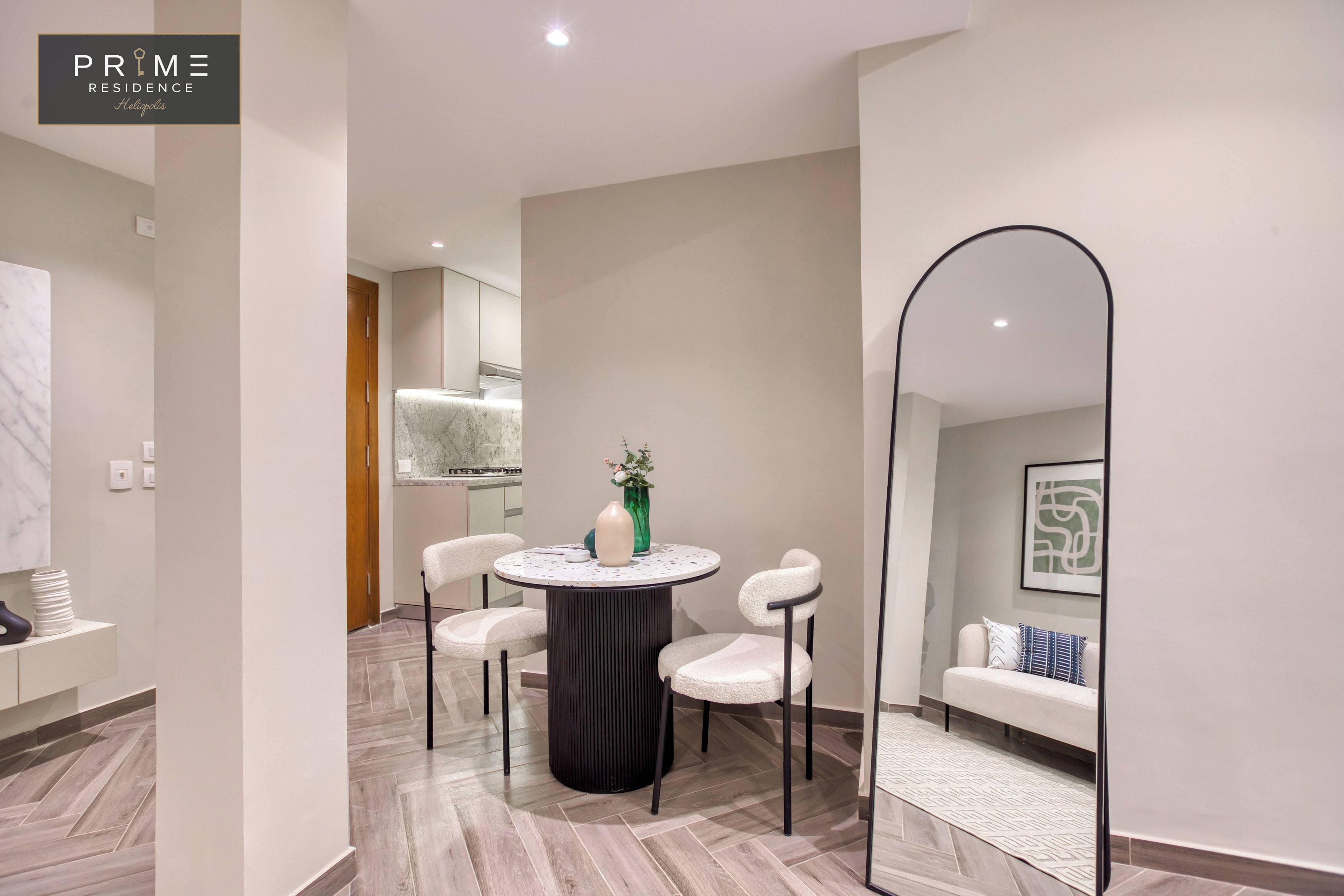 A modern living room with a round table, two white chairs, a sofa, and a large mirror.