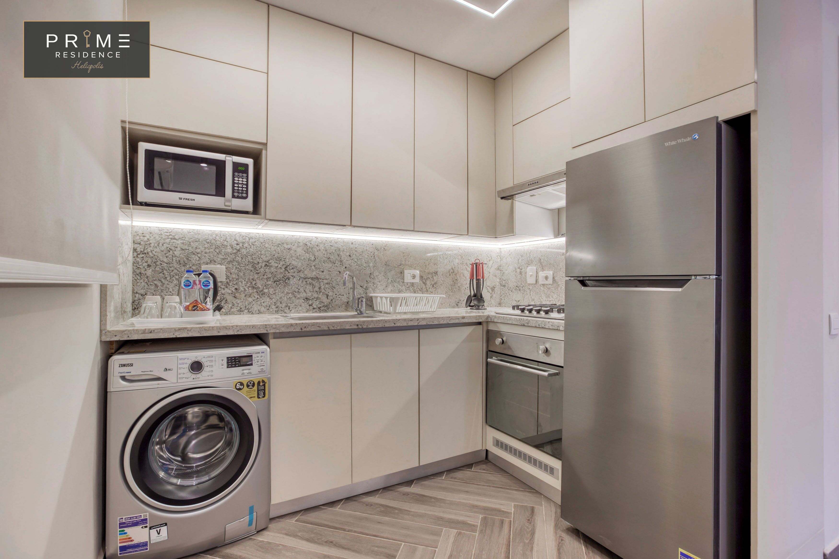 Una cocina moderna con lavadora integrada, microondas y refrigerador de acero inoxidable.