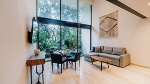 A modern living room with a large window, a round dining table, and a grey sofa. - Welcome to Mistiq Temple II in Tulum, where modern luxury meets the natural beauty of the region (Tulum)