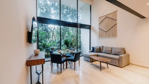 A modern living room with a large window, a round dining table, and a grey sofa. - Welcome to Mistiq Temple II in Tulum, where modern luxury meets the natural beauty of the region (Tulum)