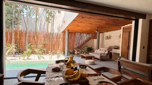 A dining area with a view of a pool, wooden furniture, and a bamboo fence. - This villa is a 2 bedroom(s), 2.5 bathrooms, located in Tulum, Quintana Roo. (Tulum)
