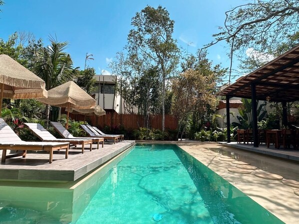 A swimming pool with lounge chairs and umbrellas, surrounded by tropical vegetation. - This villa is a 2 bedroom(s), 2.5 bathrooms, located in Tulum, Quintana Roo. (Tulum)