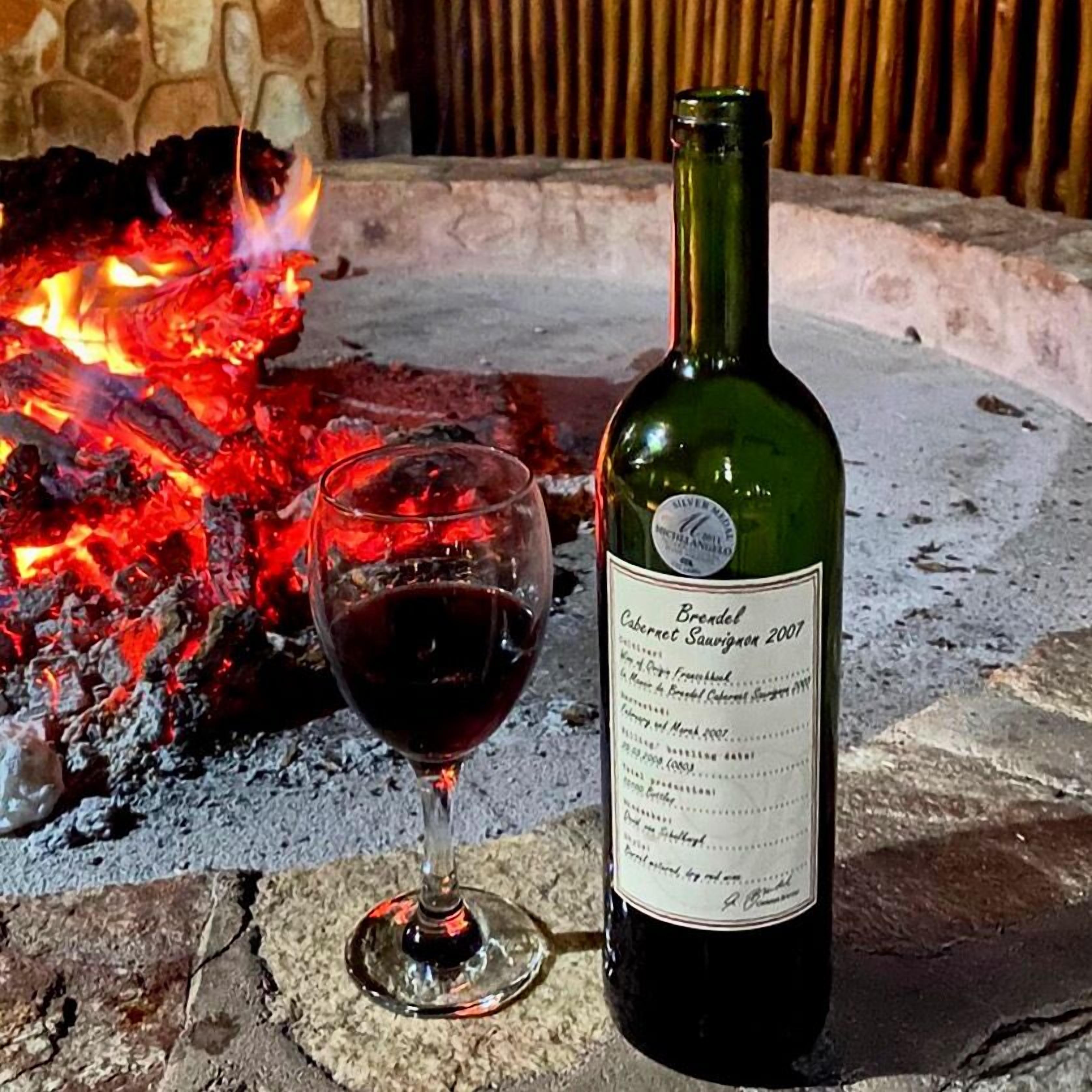 Une bouteille de Brendel Cabernet Sauvignon, millésime 2007, et un verre de vin rouge, posés devant un feu.