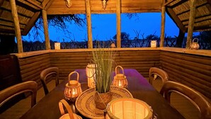 Ein Innenraum mit einem Holztisch, Stühlen, Laternen und Blick durch ein Fenster.