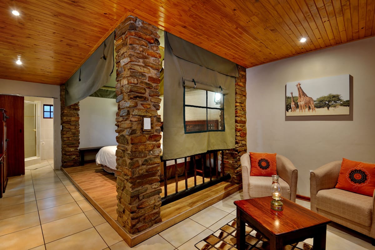 Una habitación con chimenea de piedra, una cama, un sofá y un cuadro con jirafas en la pared.