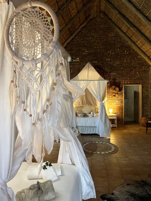 A cozy bedroom with a canopy bed, a dreamcatcher, and a rustic brick wall. - Gamagara Africa private nature reserve (Joe Morolong)