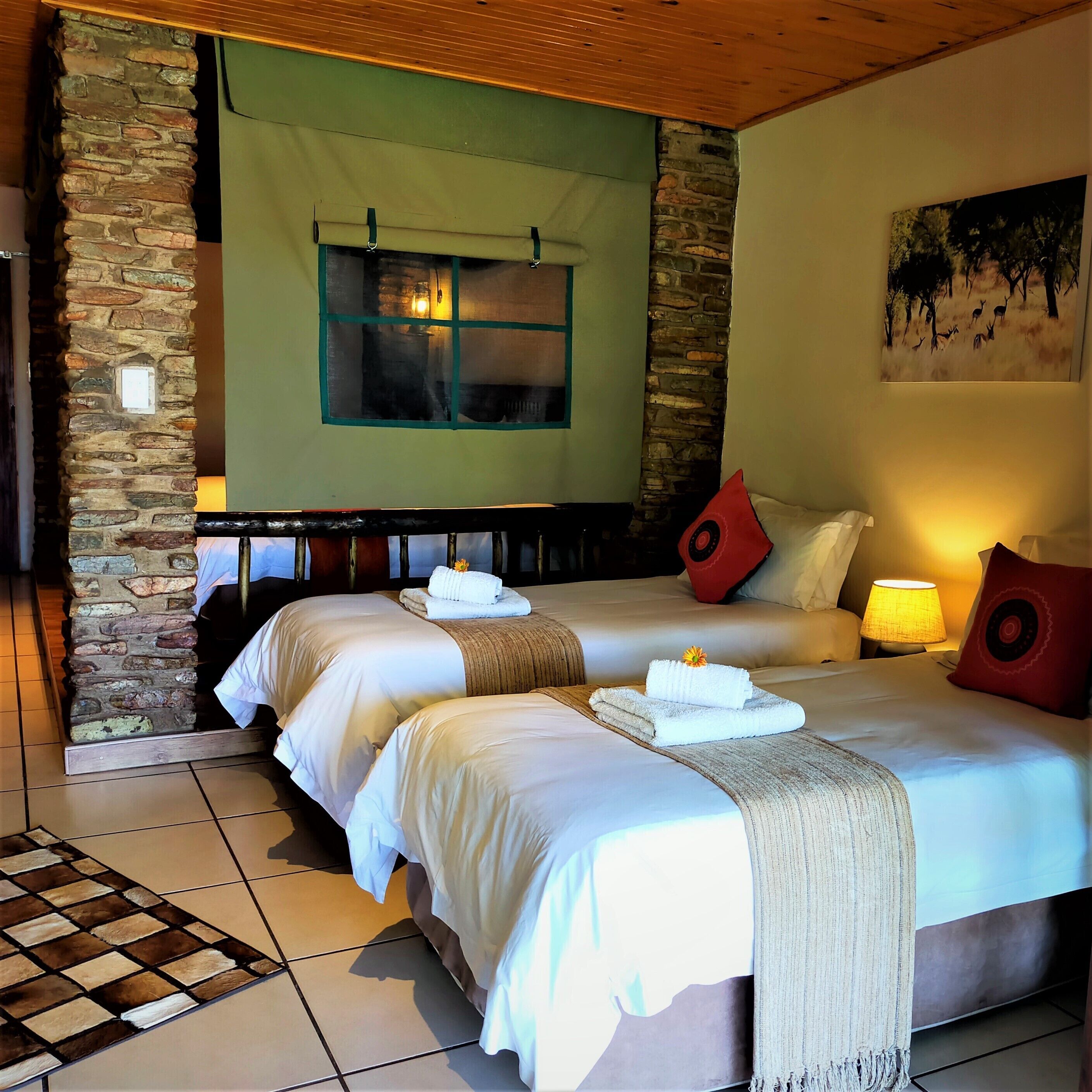 Habitación de hotel con dos camas, una pared de piedra, una ventana y un cuadro en la pared.