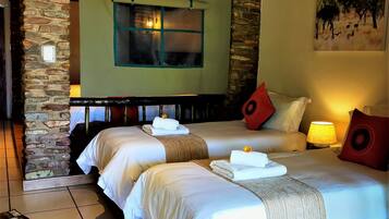 Habitación de hotel con dos camas, una pared de piedra, una ventana y un cuadro en la pared.