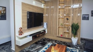 A modern living room with a large flat-screen TV, wooden panel wall, and a marble floor. - The Captains Apartment Abuja (Abuja)
