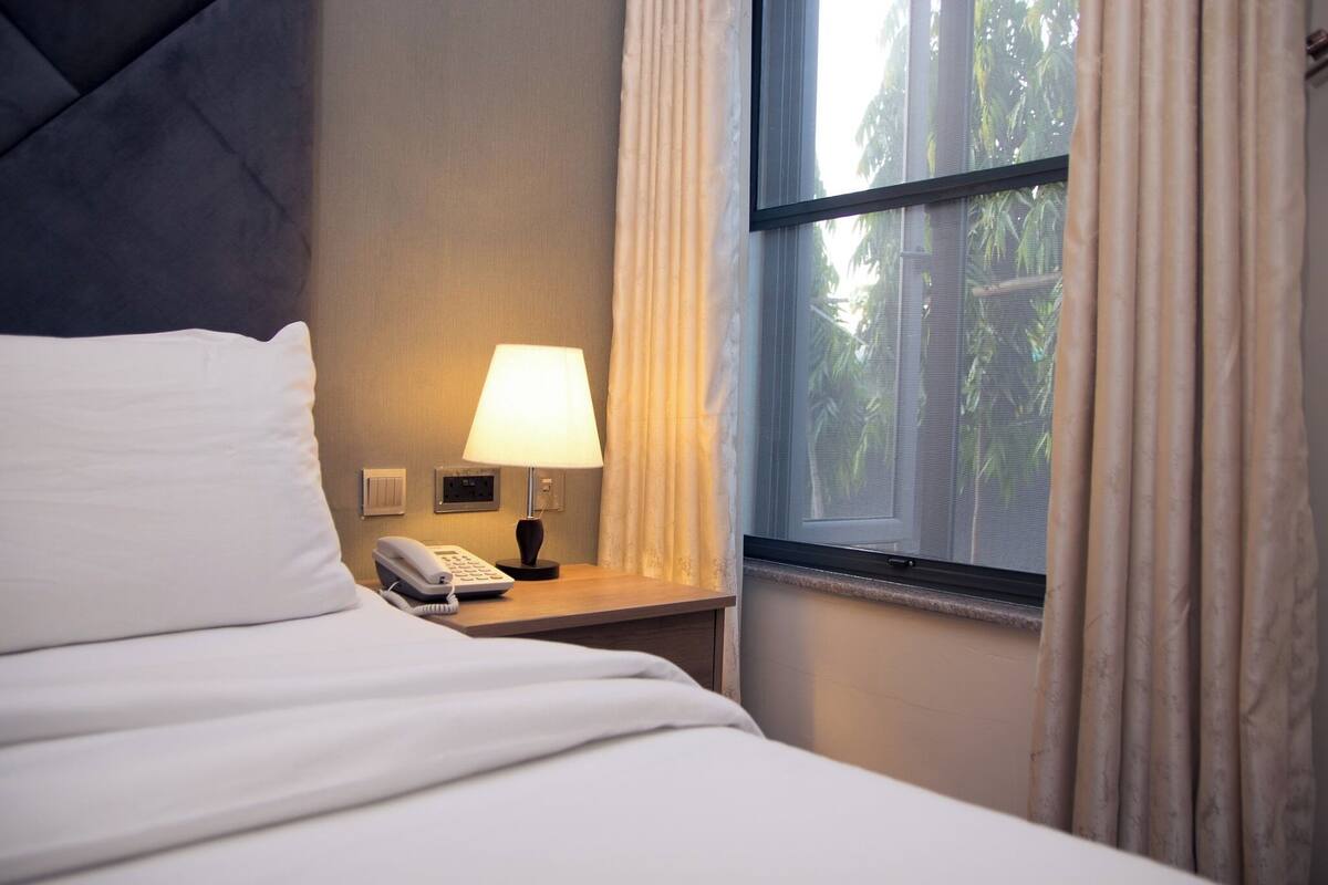 A hotel room with a bed, a bedside lamp, a phone, and a window with curtains.