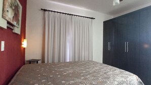 Een slaapkamer met een bed, een kledingkast, een gordijn en een aan de muur hangend schilderij.