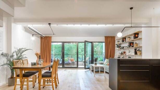 Ein geräumiger Essbereich mit einem Holztisch und Stühlen, einem weißen Sofa und einer schwarzen Schrank mit Regalen.
