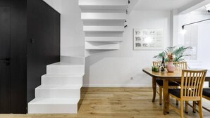 Eine Treppe führt zu einer zweiten Etage, einem Essbereich mit Tisch und Stühlen sowie einer Wand mit gerahmten Bildern.