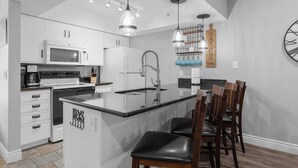 A modern kitchen with white cabinetry, a central island with bar stools, a built-in microwave, and a coffee maker. - Close to HWY 76 Strip!  Great Location! (Branson)