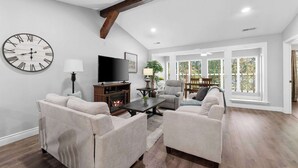 A spacious living room with a fireplace, comfortable seating, a large wall clock, and a television. - Close to HWY 76 Strip!  Great Location! (Branson)