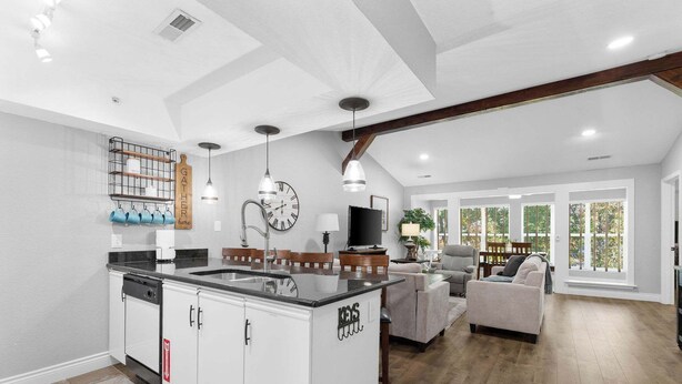 A modern kitchen with white cabinetry, a black countertop, and a built-in island. There is a dining area with a sofa and a TV. - Close to HWY 76 Strip!  Great Location! (Branson)