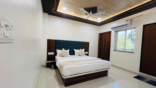 A modern bedroom with a large bed, a ceiling fan, and a window with a view of trees. - Hotel Hari Palace (Ujjain)