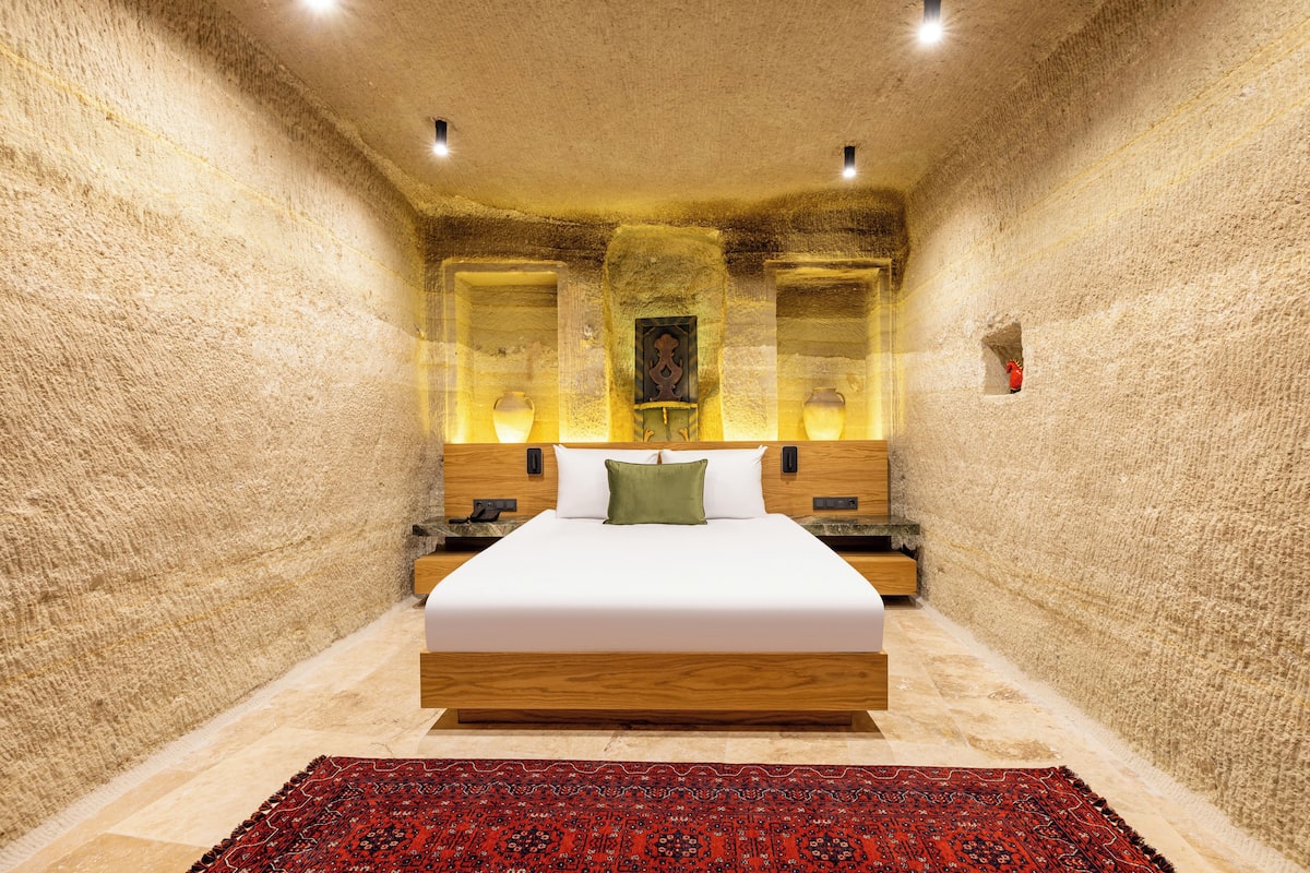 A bedroom with a large bed, wooden headboard, and a red patterned rug.