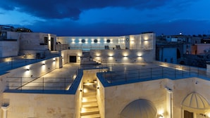 A rooftop terrace with a staircase leading to an upper level, surrounded by walls with built-in lighting and a view of the cityscape at dusk.