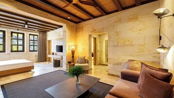A spacious living area with a sofa, a coffee table, and a TV. There is a wooden ceiling and a stone wall.