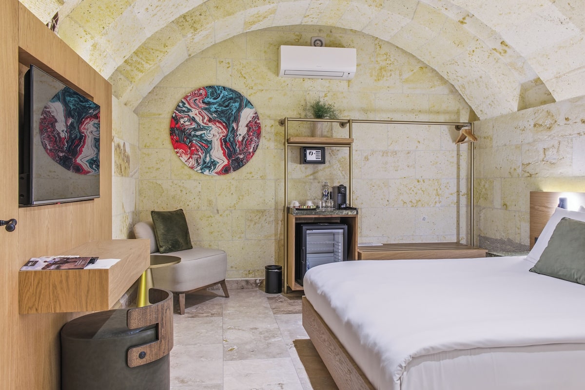 A bedroom with a bed, a desk, a chair, a small shelf, and a wall-mounted air conditioner.