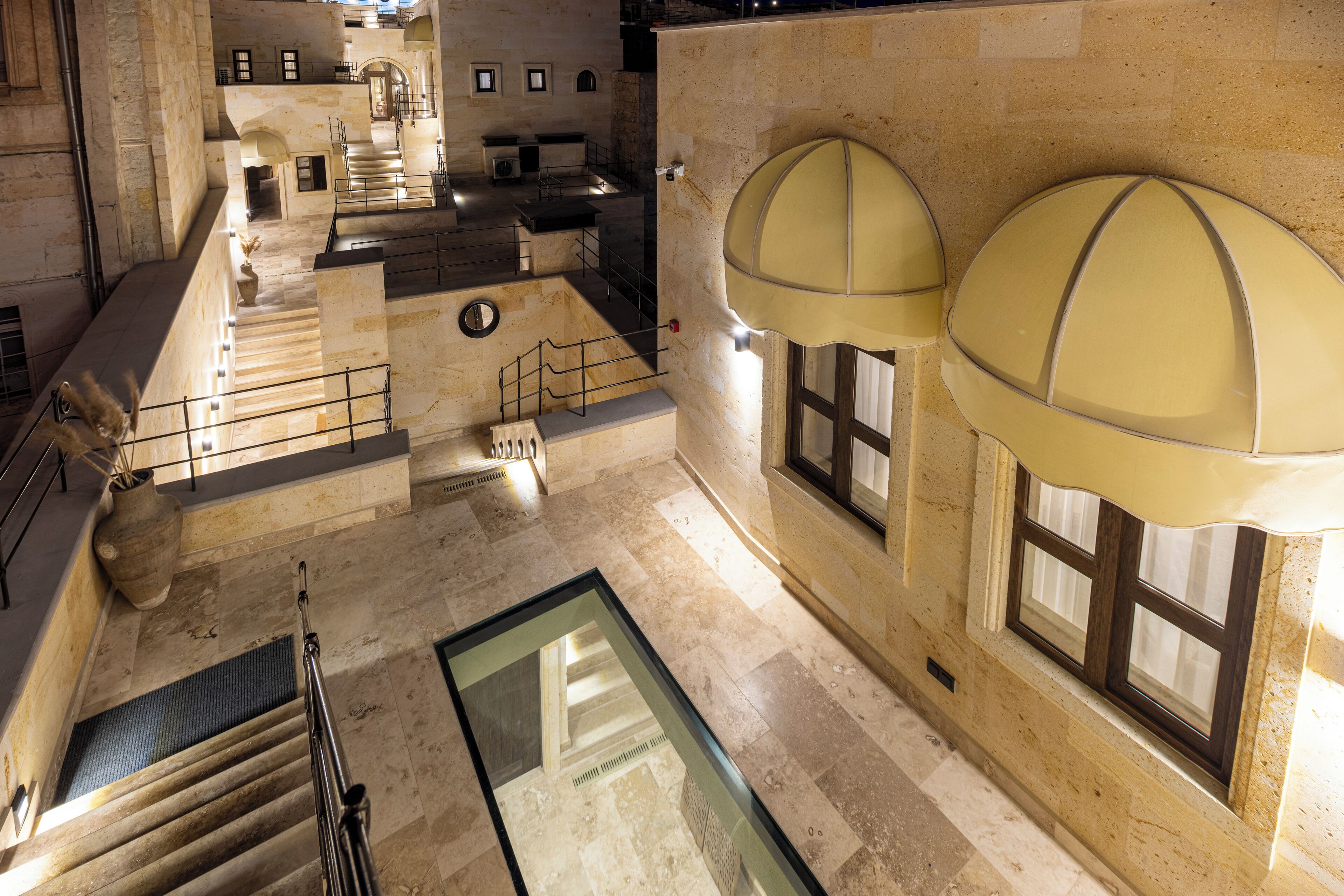 A spacious atrium with a central glass floor, stone walls, and a staircase leading to upper levels.
