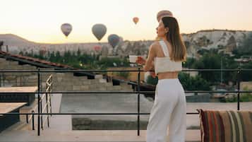 A person standing on a terrace with a table of food and drinks, overlooking a landscape with hot air balloons.