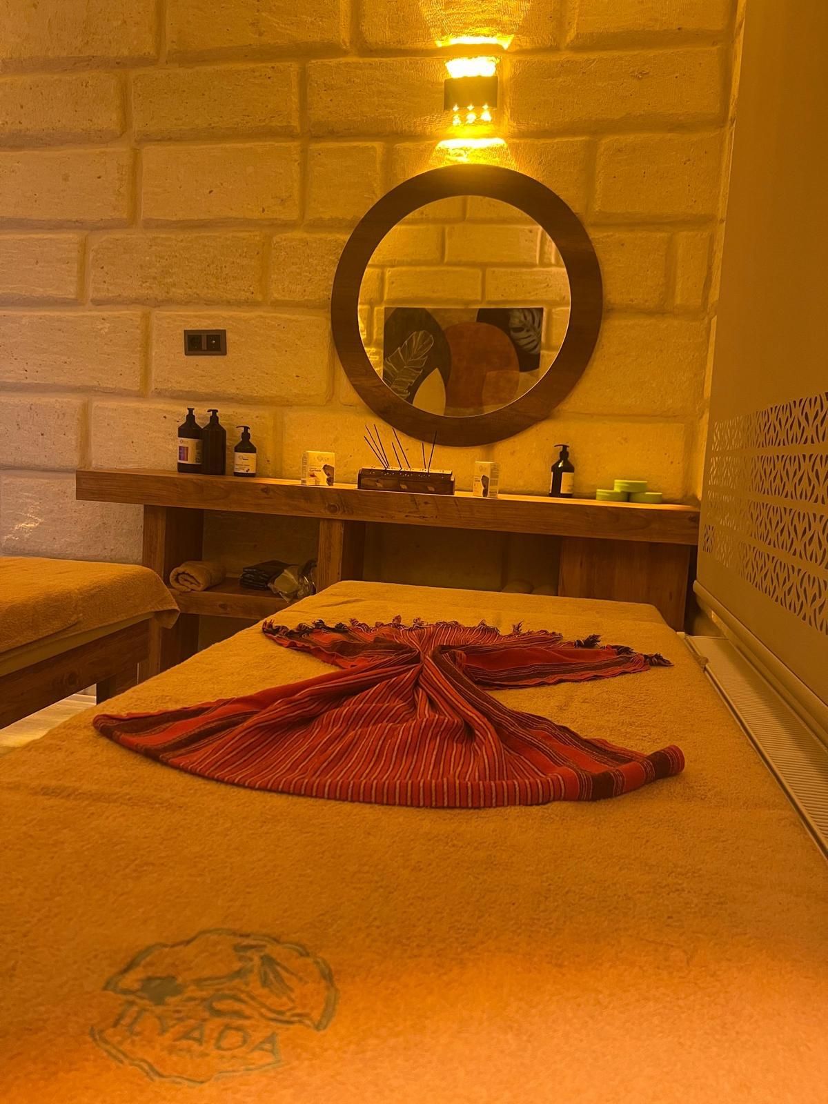 A room with a bed, a wooden bench, a mirror, and a wall-mounted shelf with toiletries.