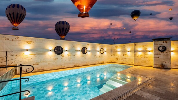 A swimming pool with a tiled floor and a stone wall, surrounded by hot air balloons in the sky.
