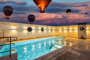 Une piscine au sol carrelé et aux murs en pierre, entourée de ballons à air chaud dans le ciel.