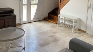 A spacious living area with a wooden staircase, a white bench, and a door with glass panels. - Accommodation La Chaumière de Rambouillet 1-6 pers (Rambouillet)