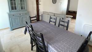 A dining area with a table and chairs, a blue cabinet, and exposed wooden beams on the ceiling. - Accommodation La Chaumière de Rambouillet 1-6 pers (Rambouillet)
